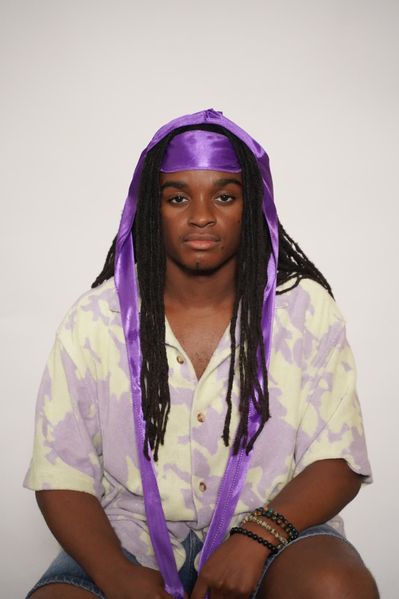 Model with long locs wearing the purple Elite Wrap, showing the flap and full-length ties